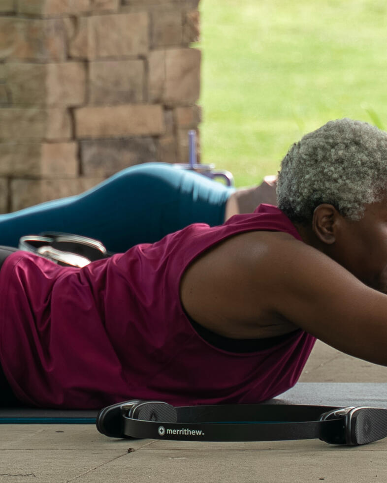 Strengthen & Lengthen Participant performing back extension exercise on mat using Pilates ball during an outdoor Pilates class.